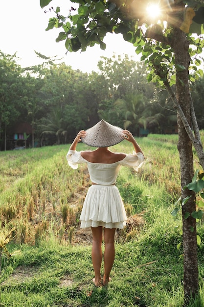 Vrouw die natuurlijke kleding en aziatische kegelhoed in het rijstveld draagt tijdens zonsondergang