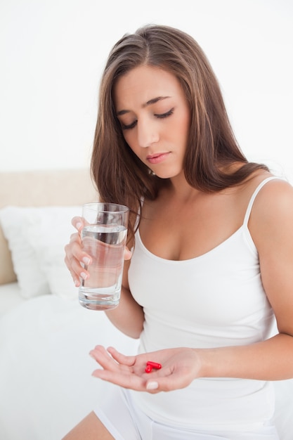 Vrouw die neer de twee pillen bekijkt die zij met water zal nemen