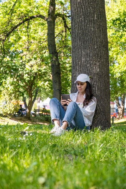 Vrouw die onder de boom zit en een elektronisch boek leest