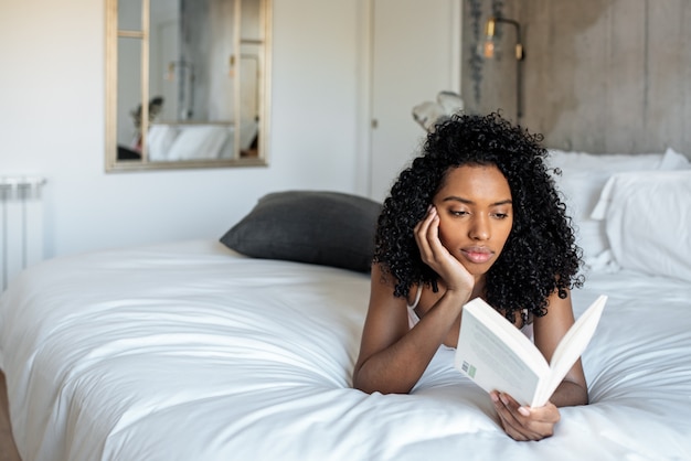 Vrouw die op bed ligt dat een boek leest