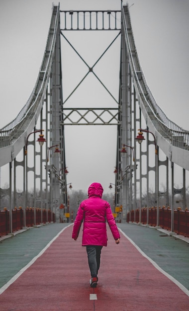 Vrouw die op de brug loopt in het roze jasje