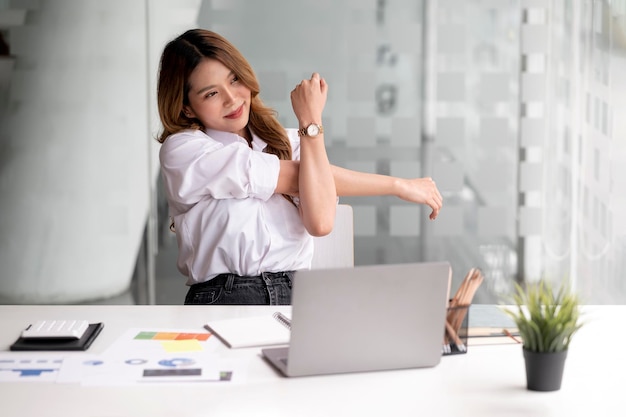 Vrouw die op de computer in het kantoor aan huis werkt en zich uitstrekt aan het bureau