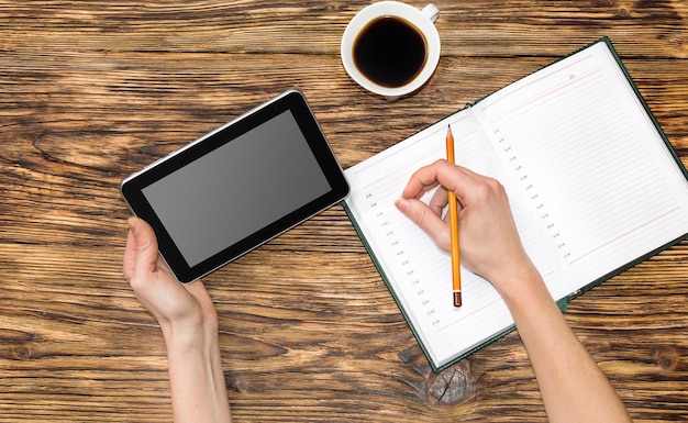 Vrouw die op de tablet-pc kijkt en informatie schrijft naar een notebook. Bedrijfs- en onderwijsconcept.