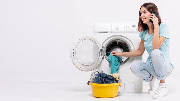 Foto vrouw die op de telefoon dichtbij wasmachine spreekt