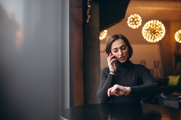 Vrouw die op de telefoon spreekt en een horloge in een koffie bekijkt