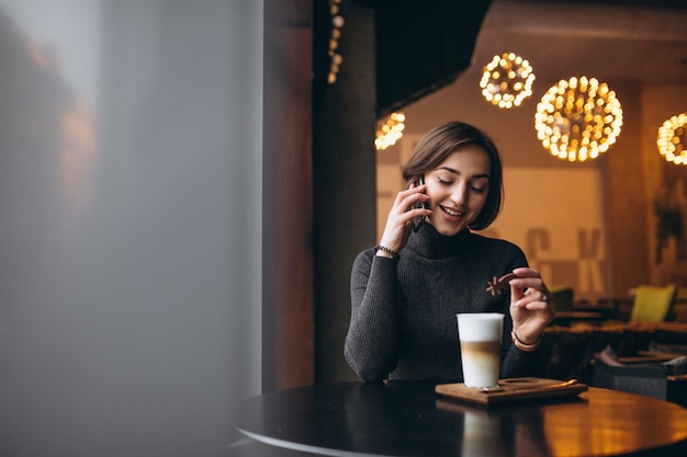 Vrouw die op de telefoon spreekt en koffie in een koffie drinkt