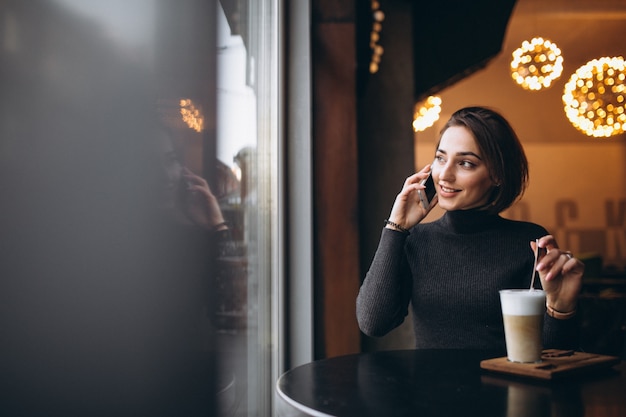 Vrouw die op de telefoon spreekt en koffie in een koffie drinkt