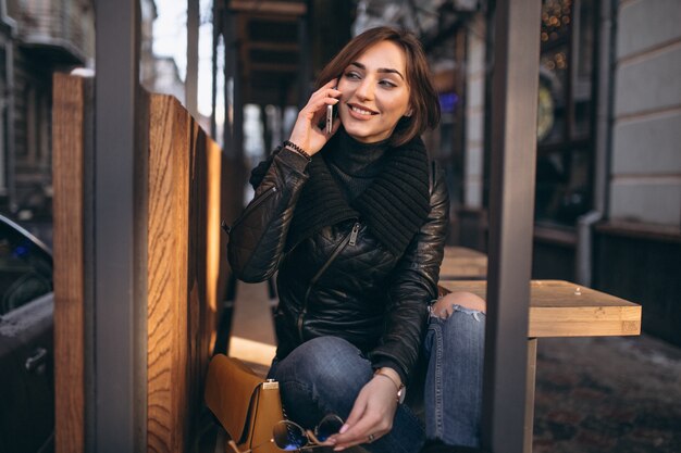 Vrouw die op de telefoon spreekt en op een bank in de straat zit