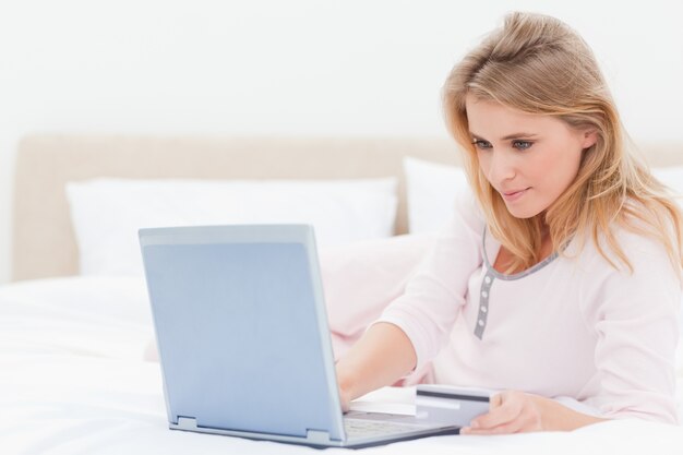 Vrouw die op een bed met haar laptop ligt, die het scherm bekijkt