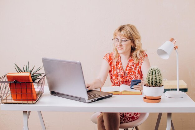 Vrouw die op een laptop werkt en een telefoon in haar hand houdt