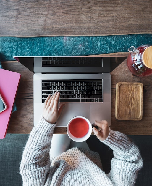 Vrouw die op een laptop werkt in een café met een kopje thee bovenaanzicht