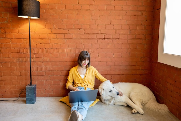 Vrouw die op een laptop werkt terwijl ze thuis met haar hond zit