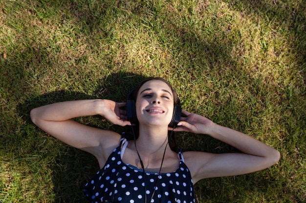 Vrouw die op gras ligt en aan muziek met hoofdtelefoons luistert