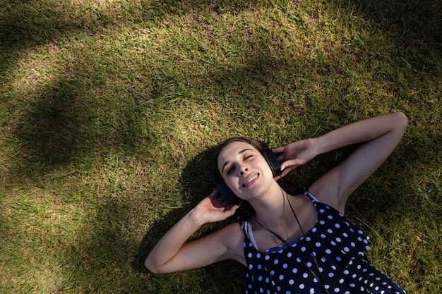 Vrouw die op gras ligt en aan muziek met hoofdtelefoons luistert