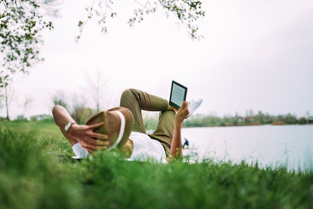 Vrouw die op grasgebied legt en e-boek leest.