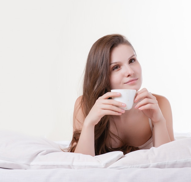 Vrouw die op haar bed terwijl het houden van een kop van koffie glimlacht