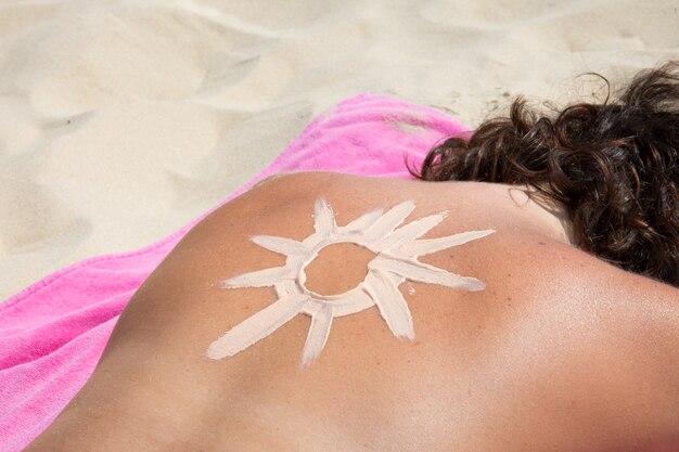 Vrouw die op het zand van het strand met een zon ligt die op de rug met zonnescherm wordt getrokken