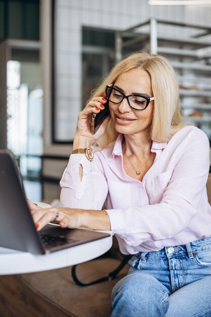 Vrouw die op laptop in een café werkt en een croissant eet