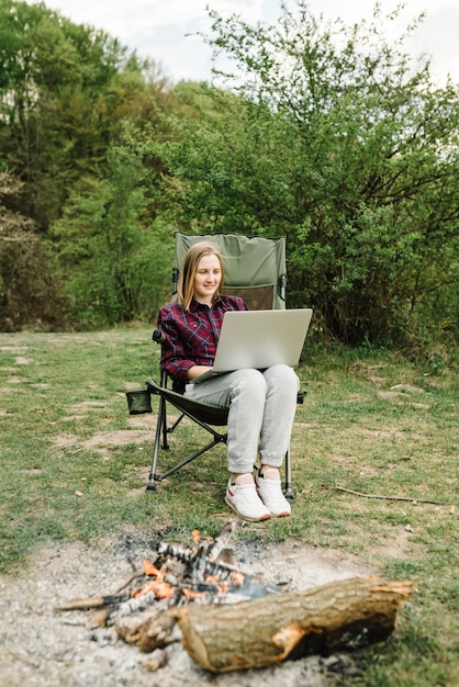 Vrouw die op laptop online aan aard werkt. Jonge freelancer ontspannen in het bos. Werken op afstand, buitenactiviteiten in de zomer. Reizen, wandelen, technologie, toerisme, mensenconcept.