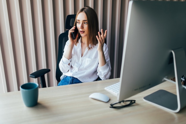 Vrouw die op laptop op kantoor werkt terwijl ze aan het telefoneren is