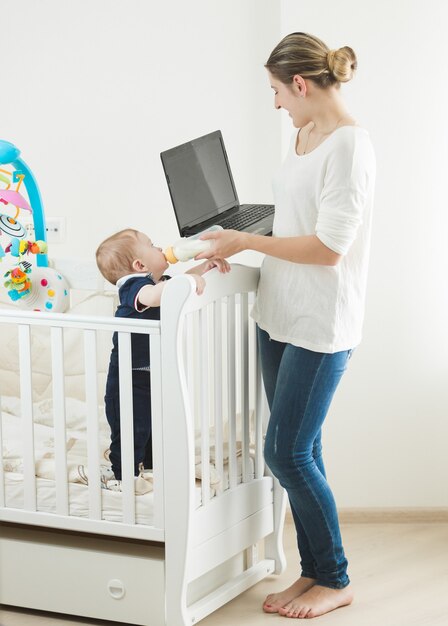 Vrouw die op laptop werkt en voor haar baby zorgt