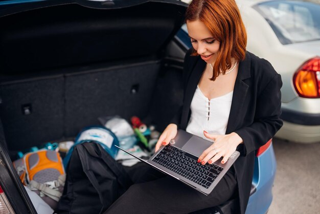 Vrouw die op laptop werkt terwijl ze in de kofferbak van de auto zit