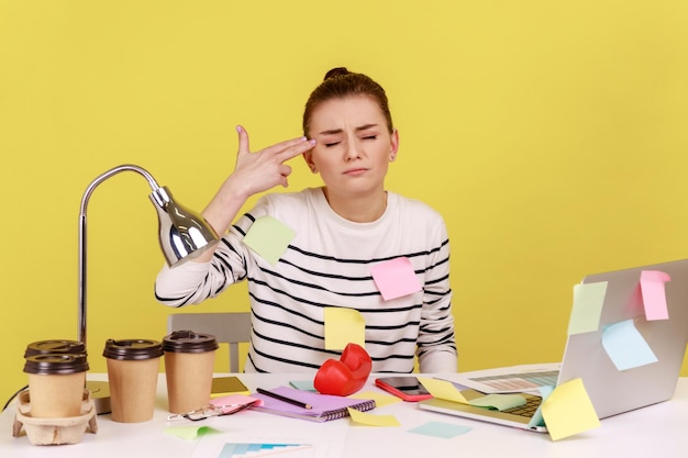 Vrouw die op laptop werkt, wijzend vingerpistoolgebaar om zelfmoord te plegen van een stressvolle baan