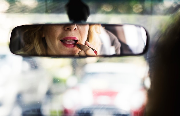 Vrouw die op lippenstift in een auto zet