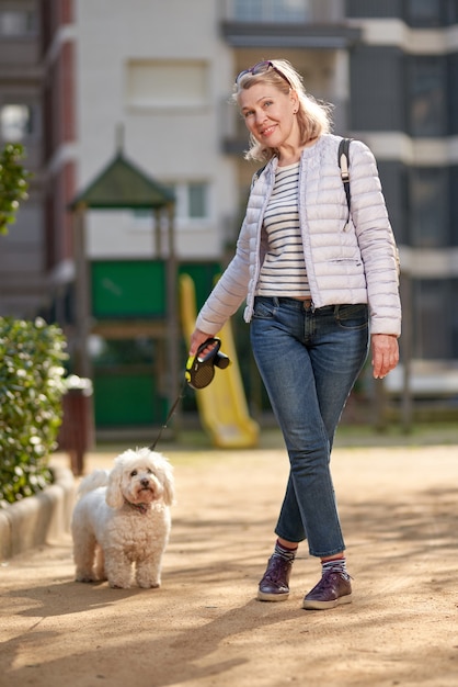 Vrouw die op middelbare leeftijd met pluizige witte hond in de zomerstad loopt