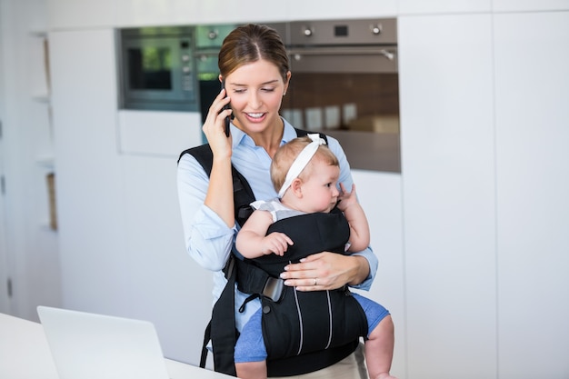 Vrouw die op mobiele telefoon spreekt terwijl het vervoeren van babymeisje