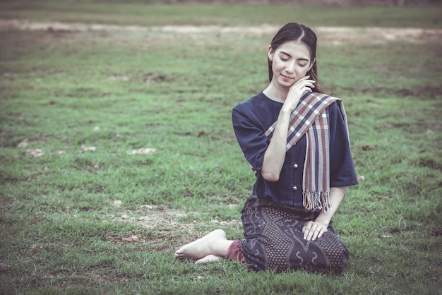 Vrouw die op Thaise traditionele kleren op het gras zit