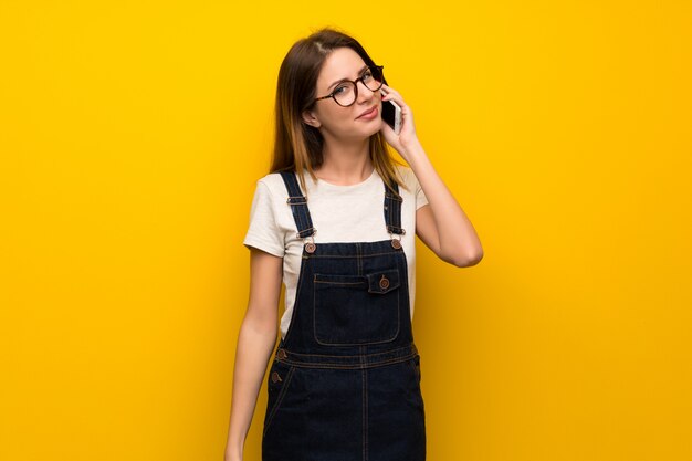 Vrouw die over gele muur een gesprek met de mobiele telefoon houdt