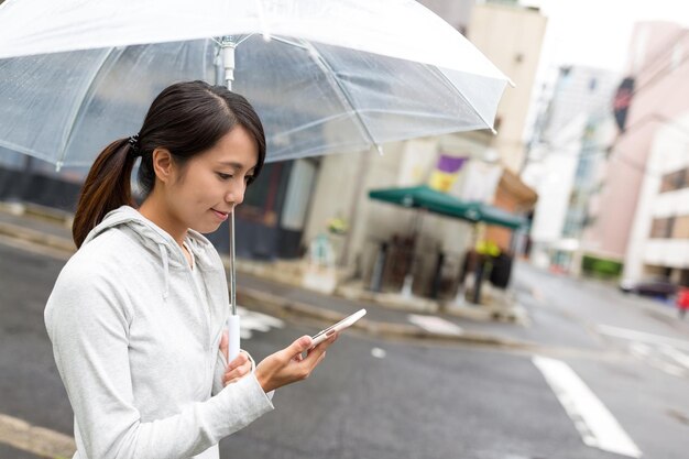 Vrouw die paraplu vasthoudt en mobiele telefoon gebruikt in de stad hiroshima