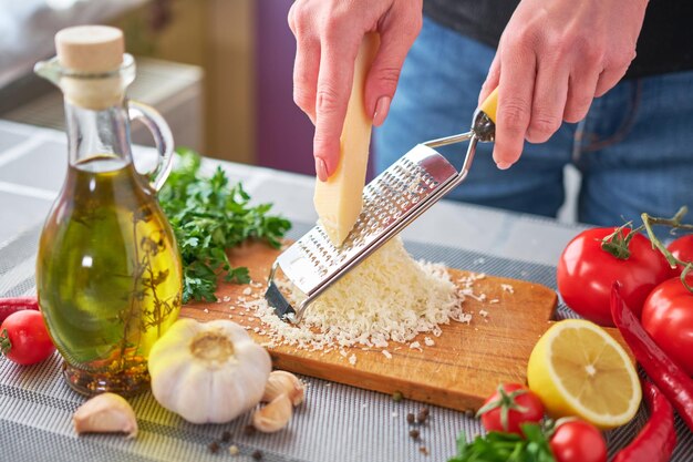 Vrouw die Parmezaanse kaas op een rasp raspt bij binnenlandse keuken