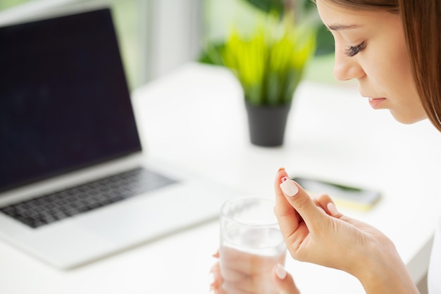 Vrouw die pil met levertraan omega3 neemt en 's ochtends een glas vers water vasthoudt