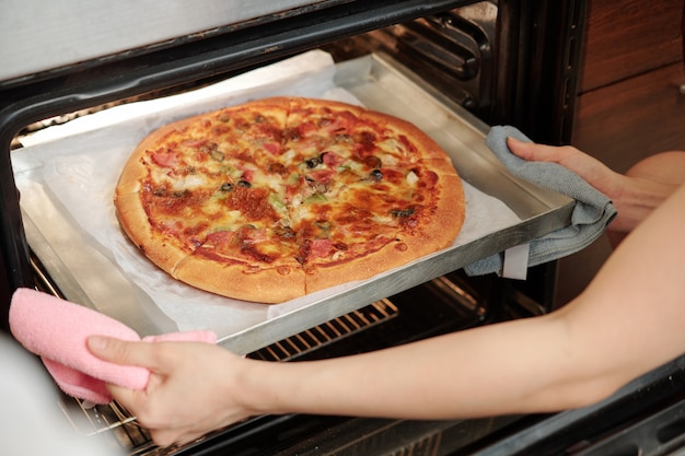 Vrouw die pizza uit de oven neemt