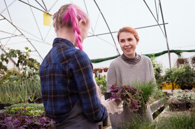 vrouw die planten kiest in de kas van het tuincentrum en een jonge bloemist die haar helpt