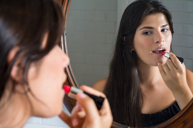 Vrouw die rode lippenstift in badkamers toepast.