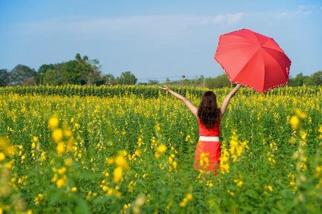 Vrouw die rode paraplu op Geel bloemgebied en bewolkte blauwe hemel houdt