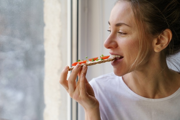 Vrouw die rogge knapperig brood met romige vegetarische kaastofu, tomaat, microgreens eet. gezond eten