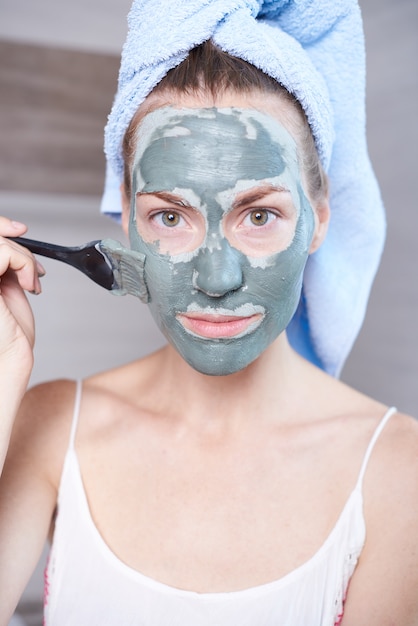 Vrouw die room van de masker de bevochtigende huid op gezicht toepassen die in badkamersspiegel kijken. Meisje het verzorgen van haar teint gelaagdheid moisturizer. Huidverzorging spa-behandeling.