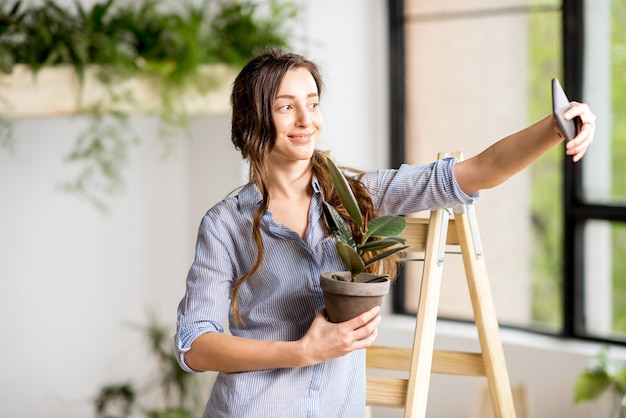 Vrouw die selfie-foto maakt die thuis met bloempot op de ladder staat