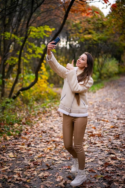 Vrouw die selfie in de herfstpark neemt jonge aantrekkelijke dame die smartphone gebruikt