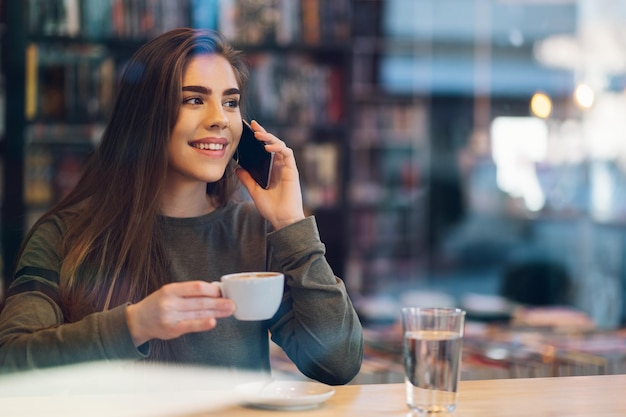 Vrouw die smartphone gebruikt en koffie drinkt in een café