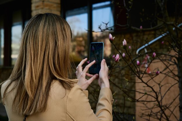 Vrouw die smartphone gebruikt om een foto te maken van de eerste magnoliabloemen in de stadsstraat