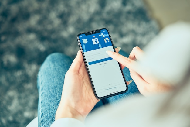 Vrouw die smartphone vasthoudt en op het facebook-scherm drukt