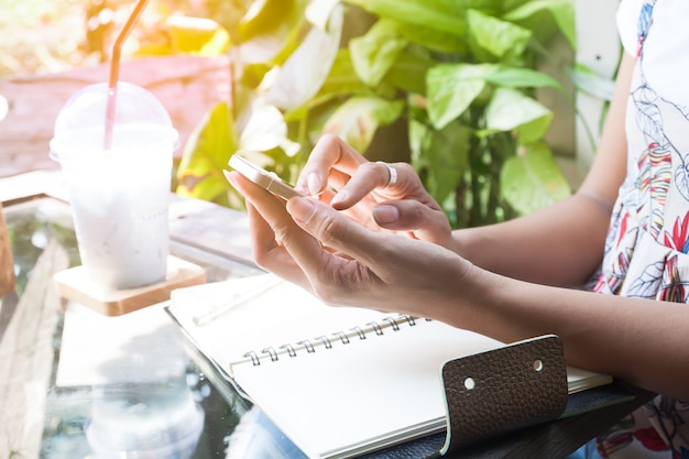 Vrouw die smartphonezitting in koffie gebruikt