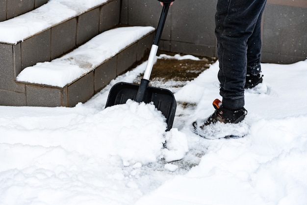 Vrouw die sneeuw van stoep schoonmaakt en sneeuwschop gebruikt.