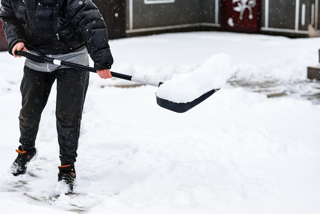 Vrouw die sneeuw van stoep schoonmaakt en sneeuwschop gebruikt.