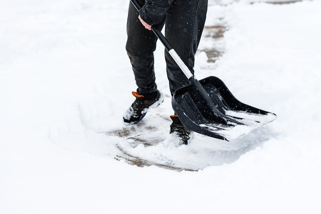 Vrouw die sneeuw van stoep schoonmaakt en sneeuwschop gebruikt.